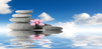 Zen stones with flower on rippling water with blue sky and clouds 